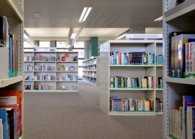 Mid Kent College Campus - Library space containing back to back Library shelving units. A view through the shelving, with books visible and book categories.
