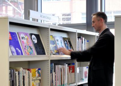 Mid Kent College Campus - A man browses the sloped section of a library shelving unit, showing a journal.