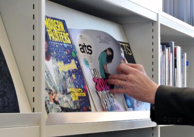 Mid Kent College Campus - Close up of Library shelving, with a hand perusing a book.