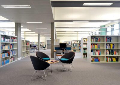 Mid Kent College Campus - Library looking across the library shelving and a seating area.