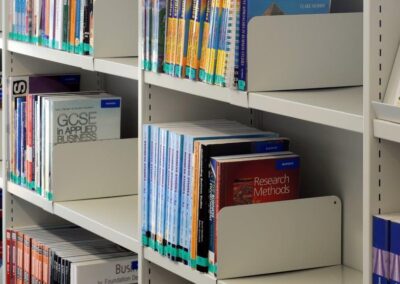 Mid Kent College Campus - Library shelving, containing books, held in place by book metal ends. The shelving is White and steel.